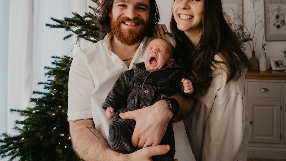 a man and woman holding a baby in front of a christmas tree